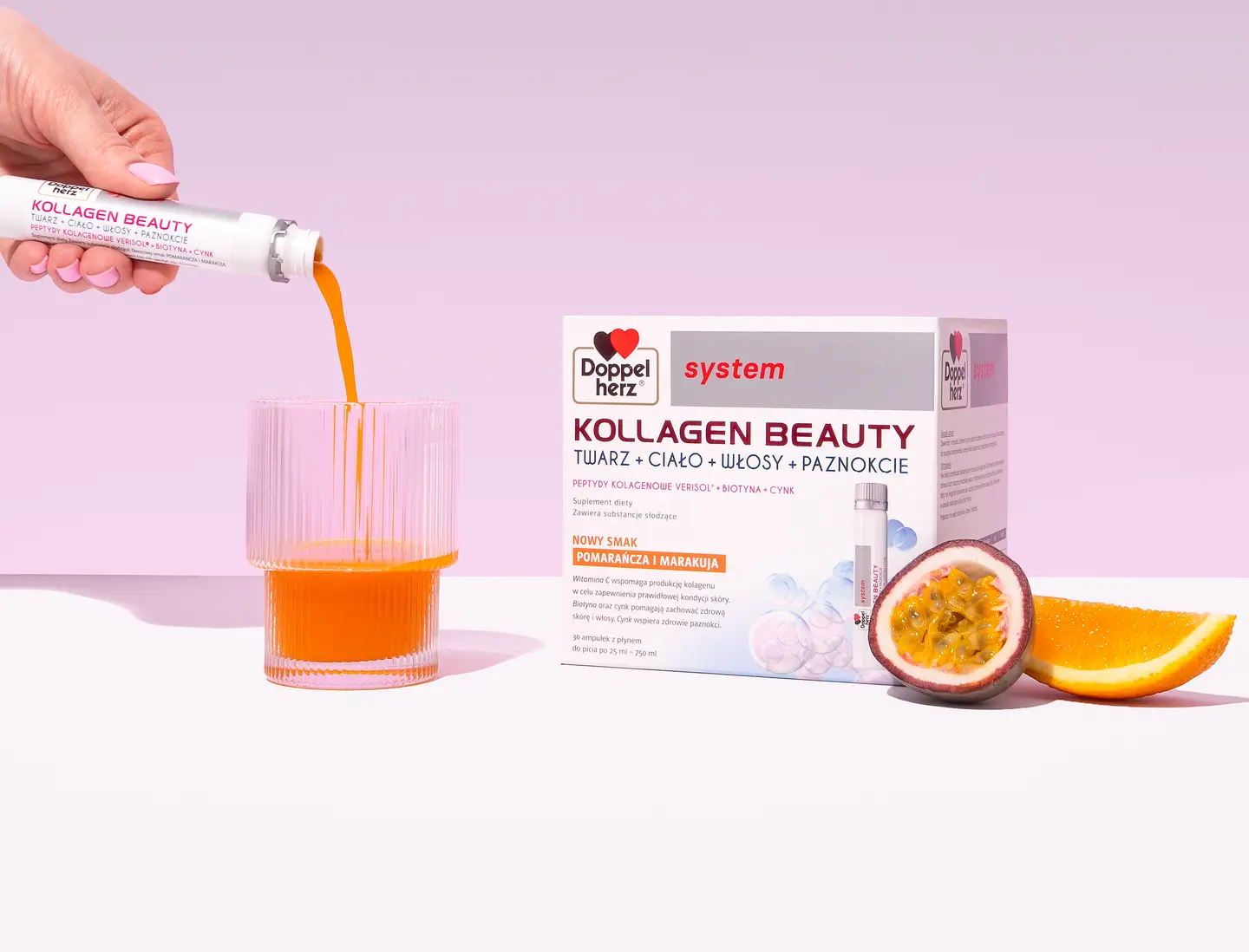 Na zdjęciu widoczna jest ręka wlewająca pomarańczowy napój z tubki do przezroczystego szklanki. Obok znajduje się opakowanie produktu "Kollagen Beauty" z logo Doppelherz oraz świeże owoce passion fruit i plasterek pomarańczy. Tło w jasnym odcieniu różowym.